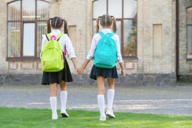 back view of two teen kids with school backpack walking together outdoor.