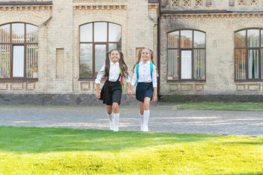 two teen girls in uniform walking together outdoor.