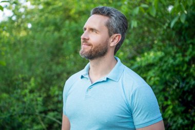 Mavi tişörtlü yakışıklı adamın portresi doğal arka plana bakıyor..