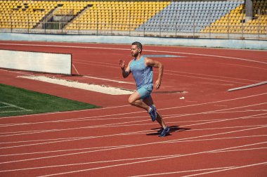 Enerjik ve sportif. Maraton hız enerjisi. Kaslı adam hareket halinde. Atletik adam sprint 'te yarışıyor. İlk ol. Spor, sağlıklı yaşam tarzı. Spor salonu açık havada. Koşucu pistte hızlı koşar.