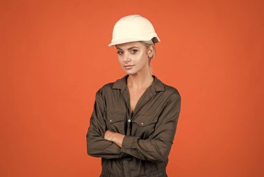 Klimalı ve kasklı kadın. Sert şapkalı kadın müteahhit. Bina ve inşaat. Bayan mimar. Turuncu arka planda mühendis. Ustabaşı kız güvenlik kaskı takıyor. İşçi Bayramı.