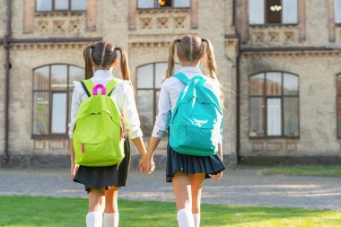 back view of two children with school backpack walking together outdoor. copy space.