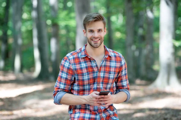 young handsome man in checkered shirt blogging on phone outdoor.