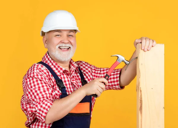 happy old aged man woodworker in helmet on yellow background.