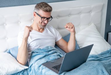 Gözlüklü olgun bir adamın laptopla yatakta çalışmasına sevindim..