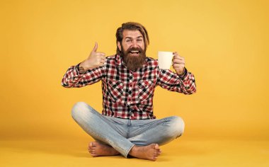 Bunu dene. Adam fincandan sıcak çay içiyor. Günaydın. Enerjik, sıcak bir içecek. İlham için kahve. Güne mükemmel bir başlangıç. Mutlu sakallı adam sabah kahvesini içiyor. En iyi tat için başparmağınızı kaldırın.