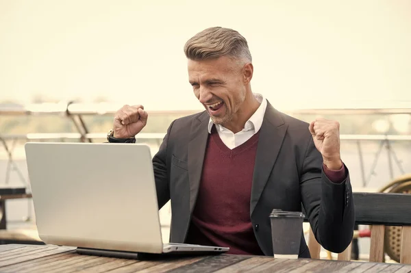 Happy professional man employee make winning gesture working on laptop outside, win.