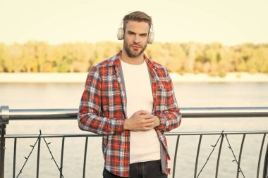 Tüylü genç adam dışarıda kulaklıkla müzik dinliyor. Erkek manken. İnternet eğitimi. Ses kitaplarını dinliyordum. Sıradan tişörtlü yakışıklı adam..