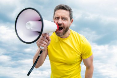 man in yellow shirt shout news in loudspeaker on sky background.