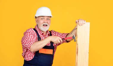 surprised senior man woodworker in helmet on yellow background.