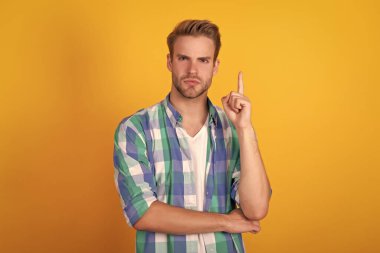 Ciddi yakışıklı, kareli gömlekli adam parmağını kaldırıp sarı arka planı işaret etmeye devam et..