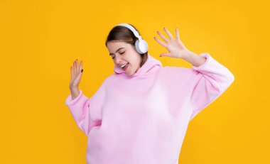 Neşeli genç kız sarı arka planda kulaklıkla müzik dinliyor..