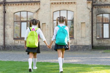 back view of two girls with school backpack walking together outdoor.