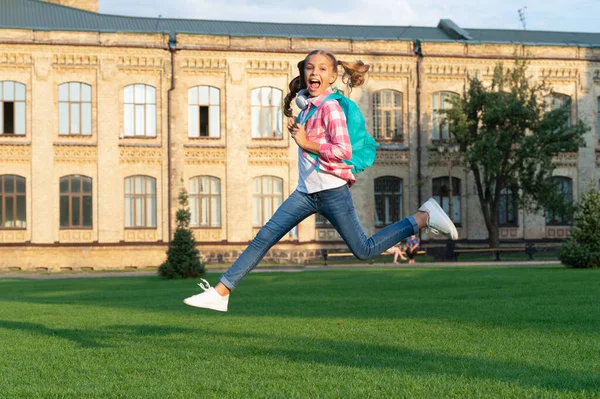 Happy teenage girl jumping in school yard outdoors, back-to-school.