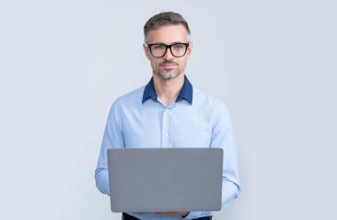 Gri arkaplanda bilgisayar üzerinde çalışan gözlüklü olgun bir yönetici.