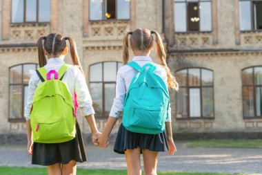 back view of two schoolkids with school backpack walking together outdoor. copy space.