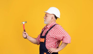 serious aged man carpenter in helmet on yellow background.