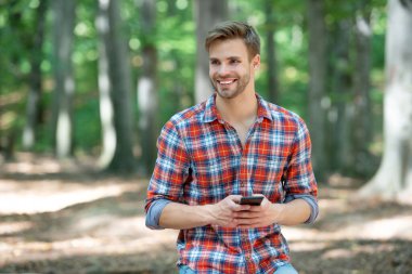 young handsome man in checkered shirt texting on phone outdoor.