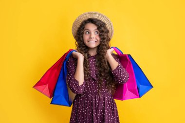 surprised girl with curly hair hold shopping bags on yellow background.