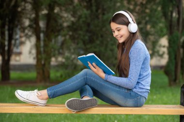 Sesli kitap konsepti. Okul çıkışı kulaklıkla okuyup dinleyen mutlu genç kız, sesli kitap..