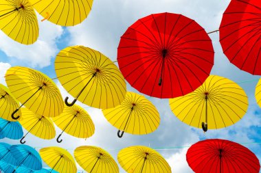 Gökyüzü zemininde asılı parlak renkli dekoratif şemsiyeler.