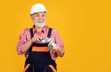 happy mature man plasterer in helmet on yellow background.