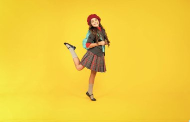 Okula dönüyorum. Bilgi günü. Eğitim konsepti. Sarı arka planda üniformalı bir çocuk. 1 Eylül. Mutlu çocukluk. Okul çantalı çocuk. Bere takmış genç bir kız sırt çantası taşıyor..