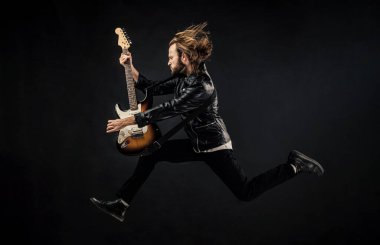 Deri ceketli duygusal sakallı rockçı. Uzun saçlı bir adam elektro gitar çalıyor. Rock müzik tarzı. Atlayan müzisyen gitarist. Rock müziğini ustaca çalmak. Modaya uygun çılgın adam. müzik aleti.