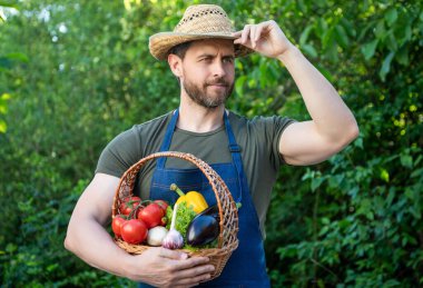 horticulturist in straw hat hold basket full of vegetables.