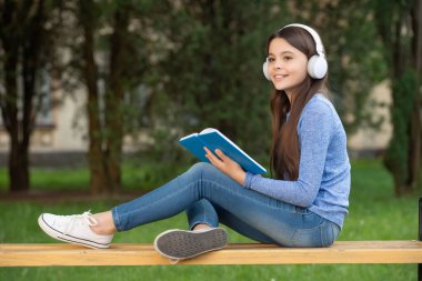 concept of teen. Happy teen girl reading and listening to audiobook in headphones after school outdoors, teen.