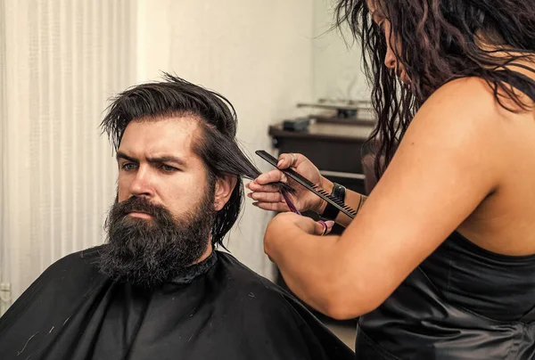 male barber care. bearded man at hairdresser chair in salon. beauty and fashion. hair and beard styling. confident brutal guy with barbershop professional master. scissors and brush for hipster.