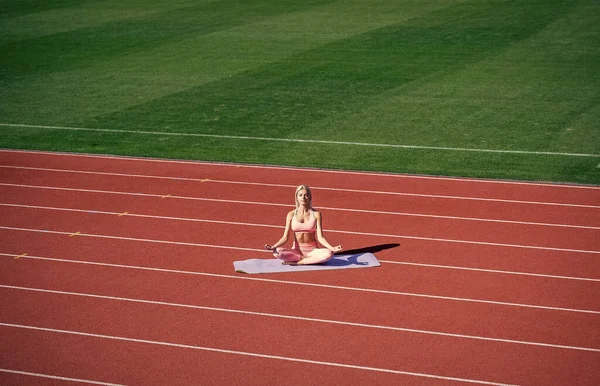 fit lady in fitness wear meditating on stadium after sport workout, yoga.