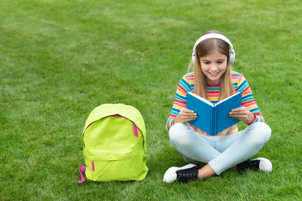 Happy Teenage Girl Reading Listening Audiobook Headphones Sitting Grass School — Zdjęcie stockowe