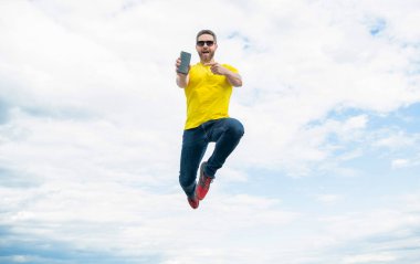 man jumping and presenting smartphone on sky background.