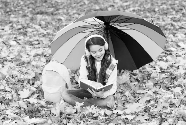 最好的嗜好回学校去戴着耳机 背包在公园里的女孩 在森林里享受秋天的乐趣 听音乐 在线课程教育 秋天的孩子在伞下 读这本书 快乐的童年 — 图库照片