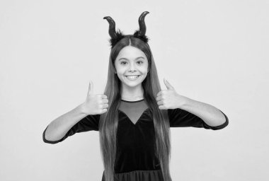 Çocuk şeytan boynuzu takıyor, baş parmağını kaldırıyor. çocukluk sonbahar tatili. Komik genç kız partiyi kutlamaya hazır. Kostüm partisi eğlencesi. Cadılar bayramın kutlu olsun. Küçük boynuzlu çocuk. mükemmel parti.