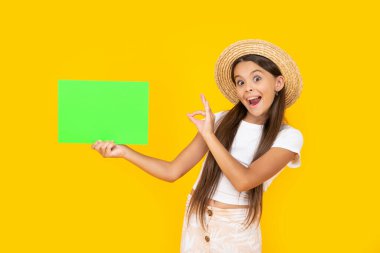 amazed teen girl with copy space on green paper on yellow background. ok.
