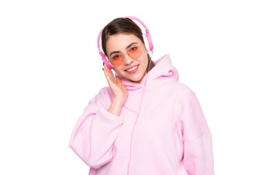 Happy girl learner in casual pink hoodie and glasses listening to online course in headphones isolated on white, e-learning.
