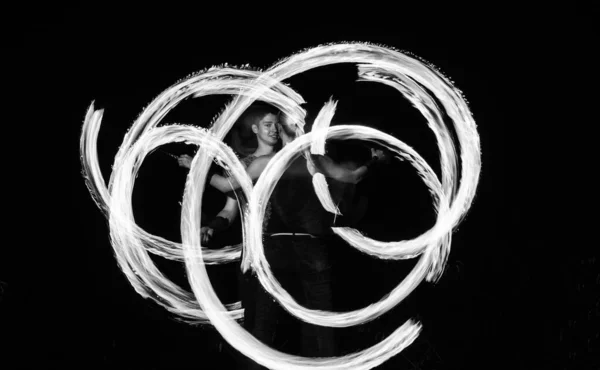 Couple of fire artists create fiery patterns spinning burning pois in night darkness outdoors, art.