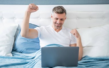 successful mature man working on laptop in bed.