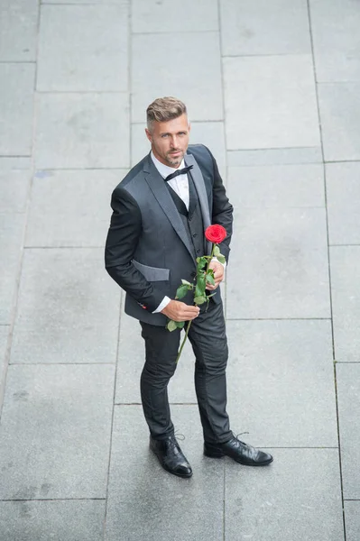 elegant man in tuxedo. man wearing bowtie suit outdoor. caucasian tuxedo man with red rose.