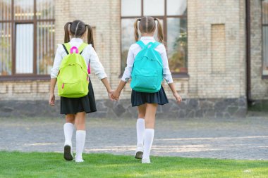 back view of two schoolgirls with school backpack walking together outdoor with copy space.