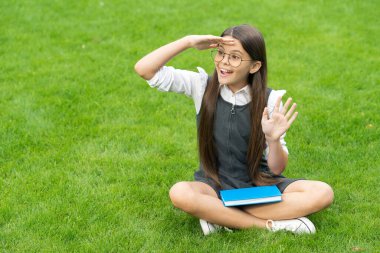 Hello school concept. Back to school. Surprised teen girl looking into distance sitting on grass, school.