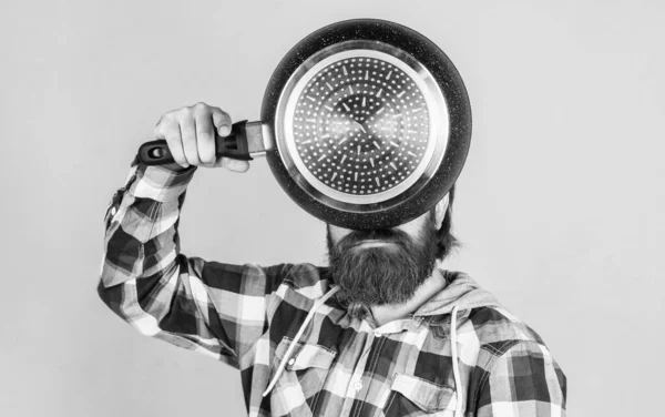 male hipster with fashionable groomed hair and beard cooking with pan, utensil.