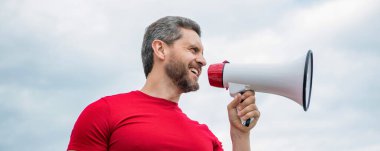 man advertiser in red shirt shout in loudspeaker on sky background.