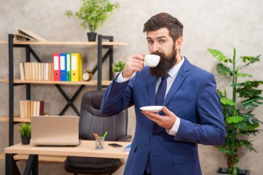 positive mature entrepreneur in jacket having coffee break at office, morning.