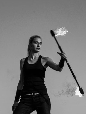 Şehvetli kadın ateş manipülatörü alevli baton çeviriyor. Açık havada mavi gökyüzü, tehlikeli..