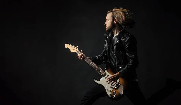 emotional bearded rock musician playing electric guitar in leather jacket and jumping, copy space, guitarist.