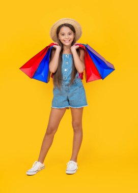 happy teen child with purchase bags on yellow background. full length.
