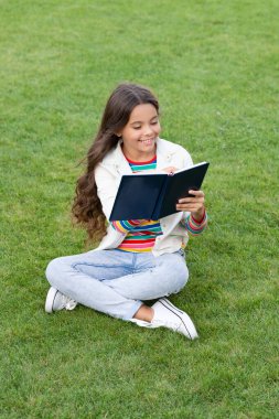 glad teen girl making notes in notebook sitting on grass. taking notes. student make notes outdoor.